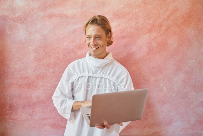 Giovane maschio felice in bianco usura con computer portatile aperto in attesa alla luce del giorno — Foto stock
