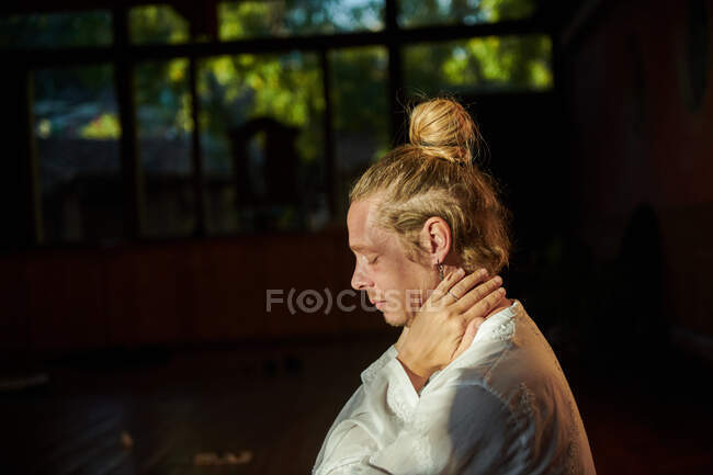 Side view of young mindful male with closed eyes and hair bun meditating in soft sunlight — Stock Photo