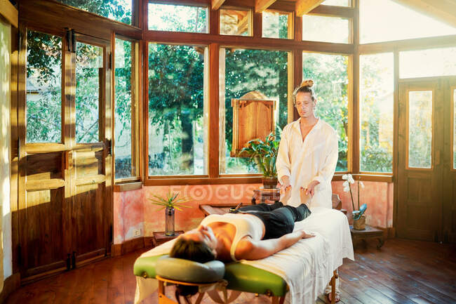 Healer practicing palm healing technique for female client lying on couch during spiritual practice for filling with harmony and energy — Stock Photo
