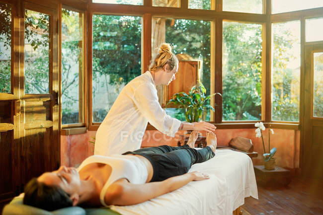 Healer practicing palm healing technique for female client lying on couch during spiritual practice for filling with harmony and energy — Stock Photo