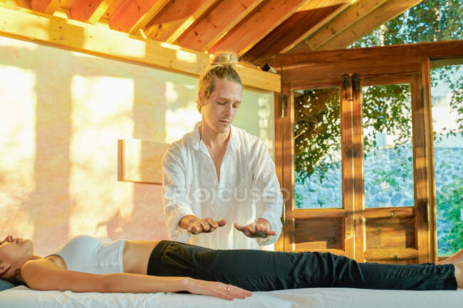 Целитель практикует технику ладони исцеления для женщины-клиента, лежащей на диване во время духовной практики для наполнения гармонией и энергией — стоковое фото