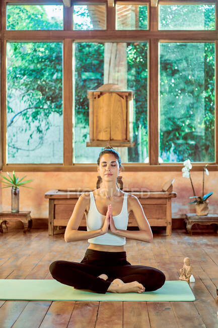 Young concentrated female with closed eyes practicing yoga with crossed legs near bowl gong in house — Stock Photo