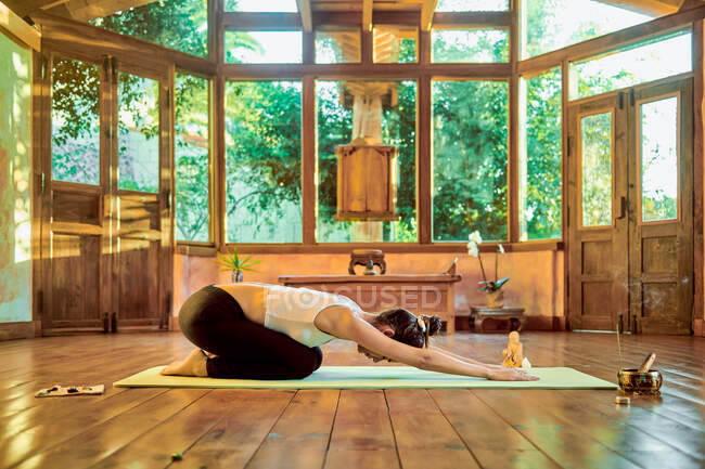 Vista laterale della donna flessibile seduta a Baddha Konasana posa durante la pratica dello yoga sul pavimento alla luce del sole — Foto stock