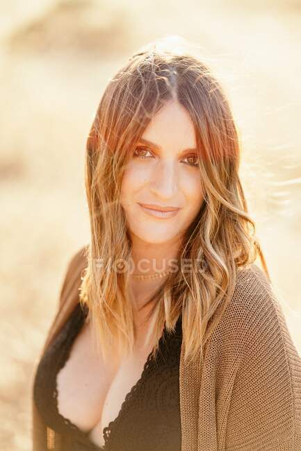 Portrait of confident woman standing in field with dry grass in sunny day and looking at camera — Stock Photo