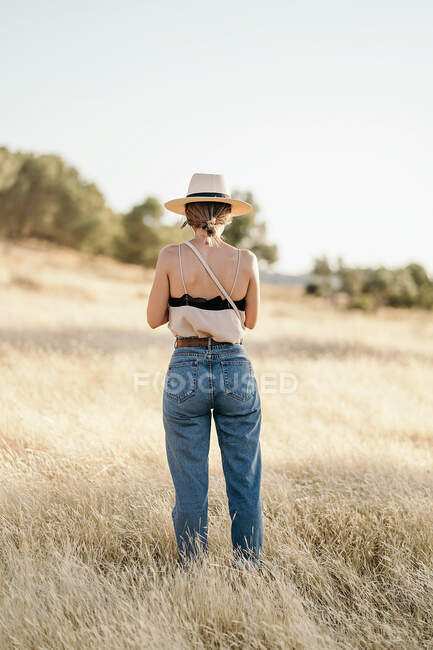 Back view of anonymous young woman standing in field with dry grass in sunny day — Stock Photo