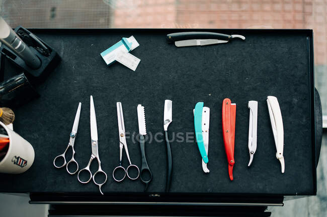 Вид зверху на різноманітні ножиці біля прямих бритв з гострими металевими лезами на столі в перукарні — стокове фото