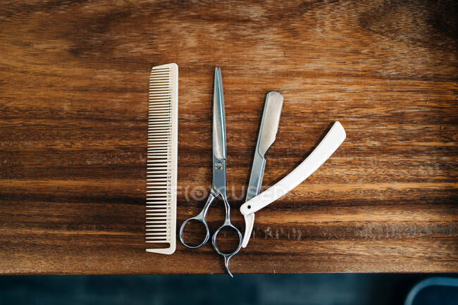 Вид зверху на ножиці і гребінець біля прямої бритви з гострими металевими лезами на дерев'яному столі в перукарні — стокове фото