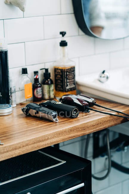 Collection of professional electric clippers near bottles of cosmetic products and washbasin in bathroom of barbershop — Fotografia de Stock