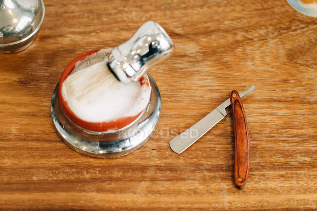 Зверху щітка для гоління з м'якою щетиною в мисці з пінистим милом біля прямої бритви на дерев'яному столі — стокове фото