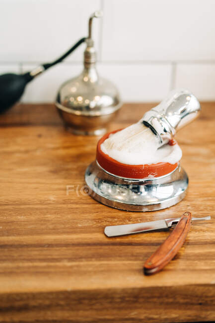 Von oben Rasierpinsel mit weichen Borsten in Schüssel mit schaumiger Seife in der Nähe von Rasiermesser auf Holztisch — Stockfoto