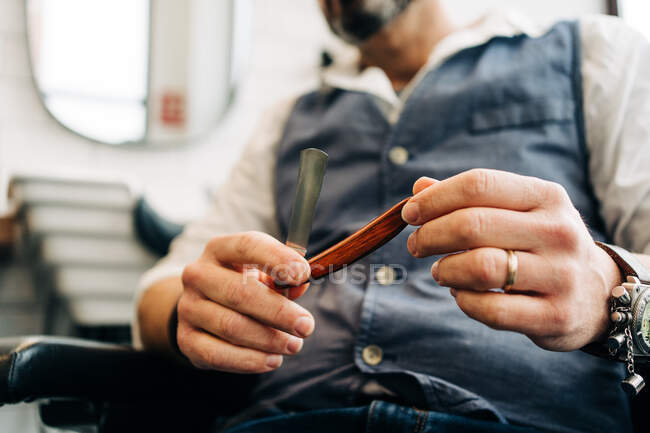 Crop unrecognizable male stylist holding straight razor with sharp blade in beauty salon in daytime — Fotografia de Stock