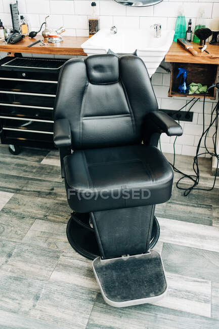 De dessus de fauteuil en cuir contre lavabo et tables avec instruments professionnels dans le salon de coiffure — Photo de stock