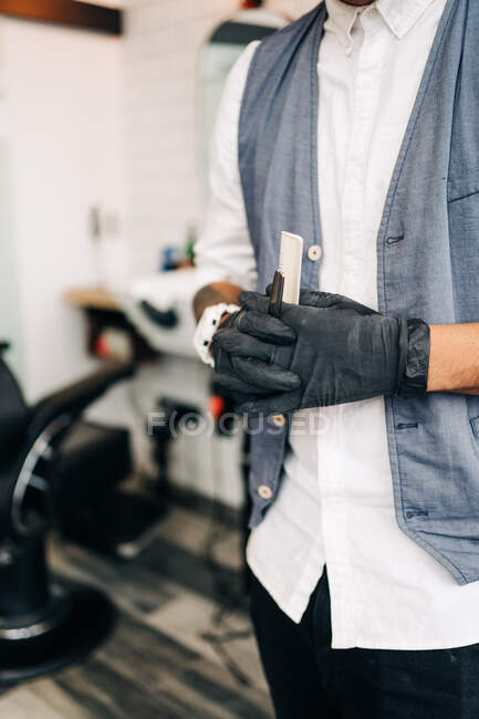 Cropped unrecognizable adult bearded male hairstylist in waistcoat standing in barbershop holding tools — Stock Photo