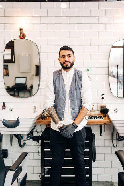 Selbstbewusster erwachsener bärtiger männlicher Friseur in Weste blickt im Friseurladen in die Kamera — Stockfoto