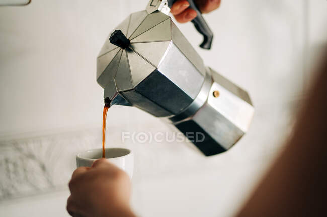 Crop anonymous person pouring hot coffee from metal stove top coffee maker into cup in house kitchen — Stock Photo