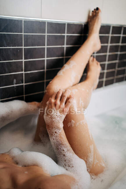 D'en haut de jeune femme séduisante couchée dans la baignoire avec de la mousse dans la maison — Photo de stock