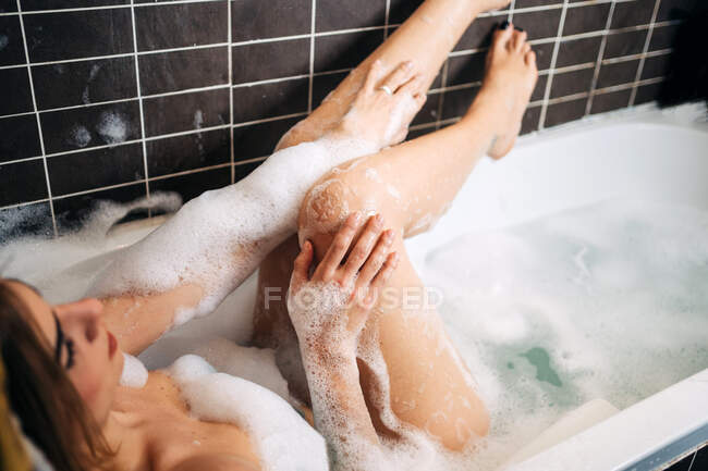 Desde arriba de joven seductora hembra acostada en bañera con espuma en casa - foto de stock