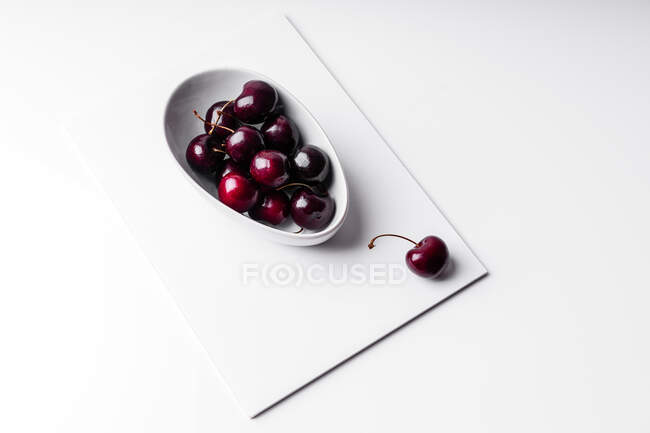 Высокий угол здоровой спелые вкусные вишни в керамической миске помещены на белой доске — стоковое фото