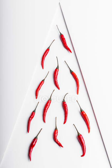 Alta composizione angolare di peperoncini rossi caldi disposti piatto contro sfondo superficie geometrica bianca — Foto stock