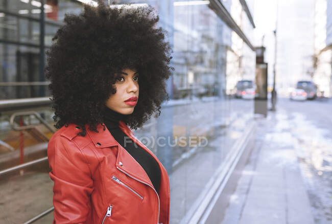 Fill body side view of confident African American female with Afro hairstyle standing on sidewalk and looking away — Stock Photo