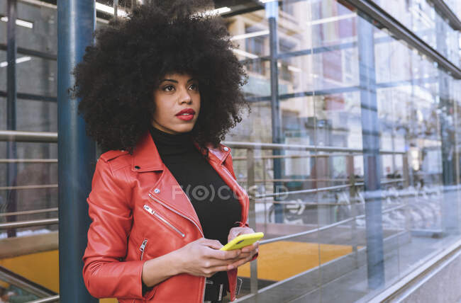 Llenar la vista lateral del cuerpo de la mujer afroamericana segura con peinado afro de pie en la acera y mirando hacia otro lado - foto de stock