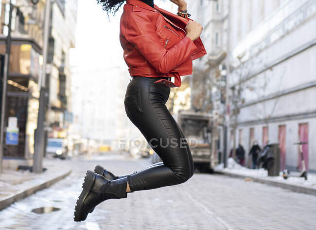 Side view of crop anonymous ethnic female jumping above ground on city street — Stock Photo