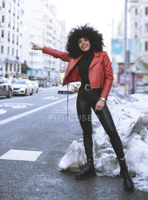 Corpo inteiro de positivo jovem afro-americano feminino vestindo roupa da moda em pé na estrada nevada e pegar um táxi — Fotografia de Stock