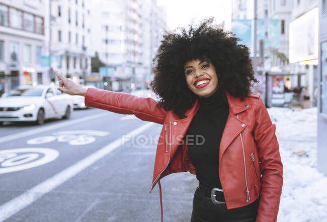 Full body of positive young African American female wearing trendy outfit standing on snowy road and catching taxi — Stock Photo