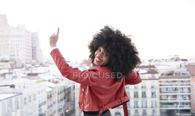 Vista posterior de la mujer afroamericana con el pelo rizado en traje elegante de pie en el balcón y mirando a los edificios de la ciudad - foto de stock