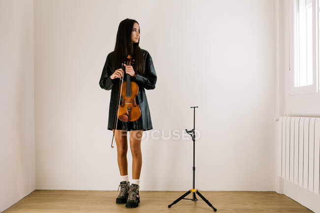 Corpo pieno di violinista donna in piedi con strumento musicale e guardando attentamente la finestra — Foto stock