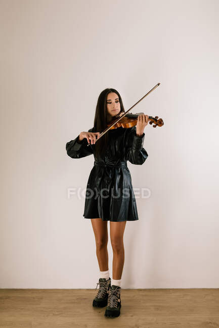 Serious artist playing stringed musical instrument while practicing skills standing against white background — Stock Photo