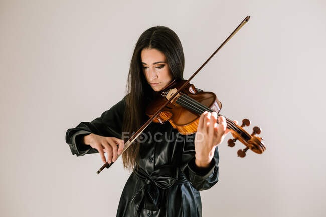 Artista sério tocando instrumento musical com cordas enquanto pratica habilidades em pé contra fundo branco — Fotografia de Stock