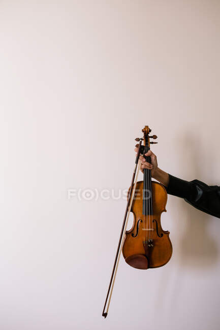 Recadrer musicien méconnaissable en soie chemise noire tenant violon acoustique moderne dans la main tendue dans la chambre — Photo de stock