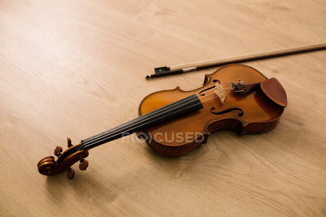 Modern acoustic violin and bow of classic design placed on wooden surface in musical studio — Stock Photo