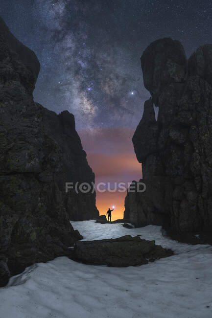 Silhouette of anonymous explorer with flashlight standing between rocky cliffs and admiring dark starry sky in Picos de Europa National Park — Stock Photo