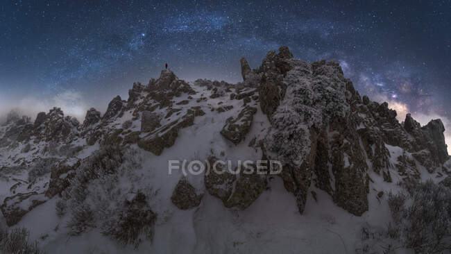 Viaggiatore in piedi sulla scogliera della catena montuosa innevata nel Parco Nazionale Picos de Europa sotto il buio cielo stellato notturno durante l'inverno — Foto stock