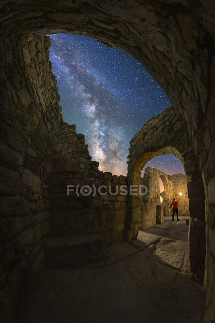 Blick zurück auf anonyme Touristin mit Laterne erkundet alte Burgruine unter Milchstraße bei sternenklarer Nacht — Stockfoto