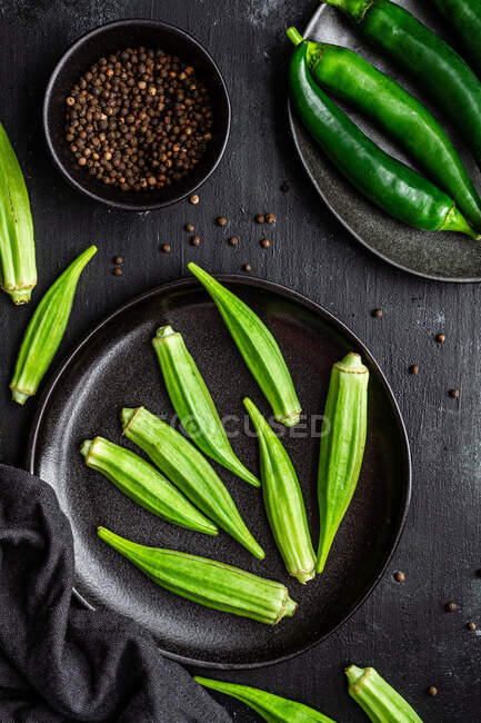 Вид зверху на стиглий зелений суперпродукт на керамічних чорних тарілках біля перцю в мисці на столі — стокове фото