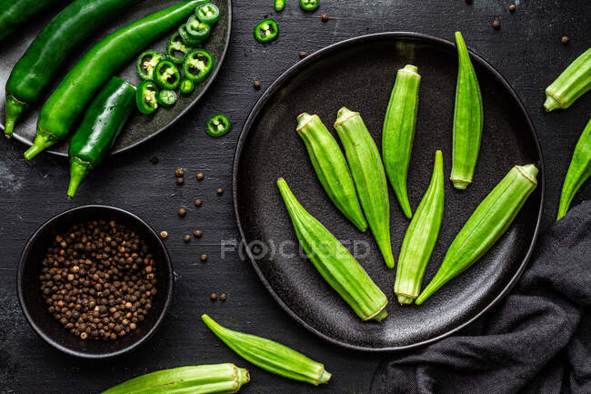 Vista superior de superalimento verde maduro em placas pretas de cerâmica perto de pimenta na tigela na mesa — Fotografia de Stock
