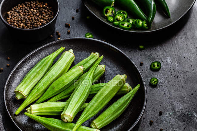 Сверху спелые зеленые суперпродукты на керамических черных тарелках возле перца в миске на столе — стоковое фото