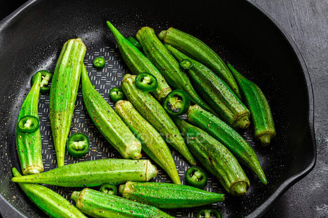 D'en haut okra frais déchiré sur poêle à frire avec poivre vert sur fond sombre — Photo de stock