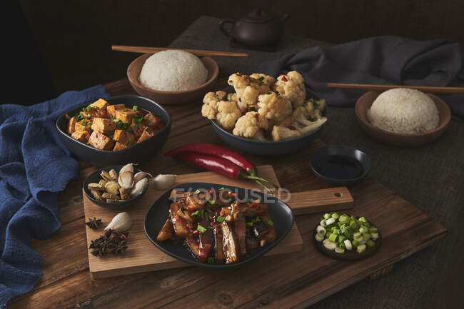 Mala Tofu und Yuxiang, chinesische vegane Gerichte, dazu eine Schüssel Reis, Blumenkohl, Sojasauce und eine japanische Teekanne auf einem mit Stoffen dekorierten Holztisch — Stockfoto