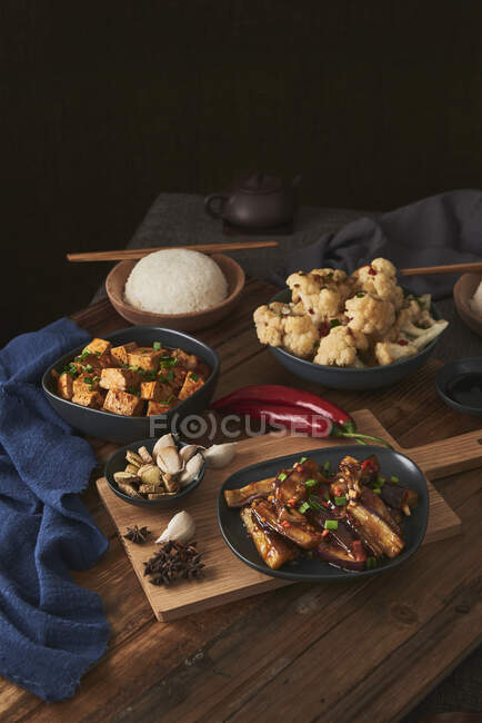 Tofu mala et yuxiang, plats chinois végétaliens, accompagnés d'un bol de riz, chou-fleur, sauce soja et une théière japonaise sur une table en bois décorée de tissus — Photo de stock