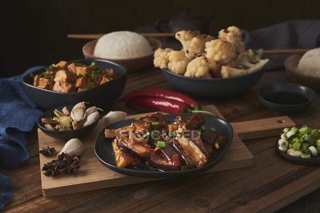 Tofu mala et yuxiang, plats chinois végétaliens, accompagnés d'un bol de riz, chou-fleur, sauce soja et une théière japonaise sur une table en bois décorée de tissus — Photo de stock