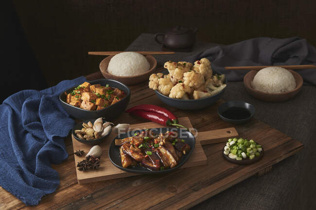 Mala tofu and yuxiang, chinese vegan dishes, accompanied by a bowl of rice, cauliflower, soy sauce and a Japanese teapot on top of a wooden table decorated with fabrics — Stock Photo