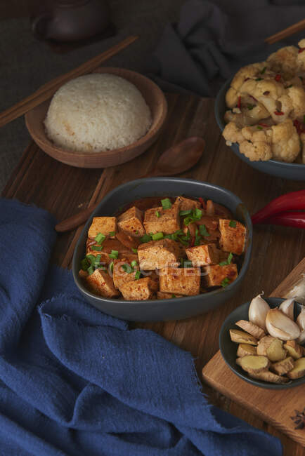 Tofu mala, piatto vegano cinese, accompagnato da una ciotola di riso, cavolfiore, salsa di soia e una teiera giapponese su un tavolo di legno decorato con tessuti — Foto stock