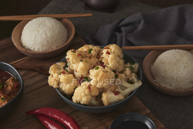Close up cauliflower dish, accompanied by a bowl of rice, soy sauce and a Japanese teapot on top of a wooden table decorated with fabrics — Stock Photo