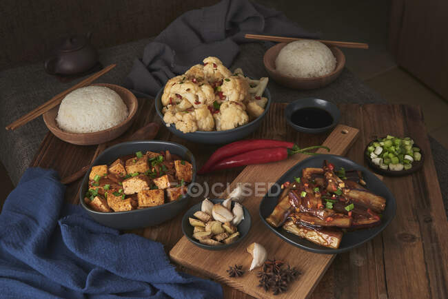 Mala tofu e yuxiang, pratos chineses vegan, acompanhado por uma tigela de arroz, couve-flor, molho de soja e um bule japonês em cima de uma mesa de madeira decorada com tecidos — Fotografia de Stock