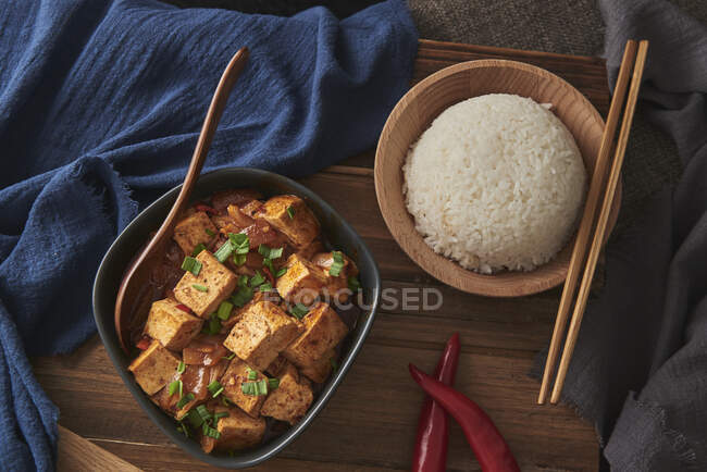 Primo piano tofu mala, piatto vegano cinese, accompagnato da una ciotola di riso su un tavolo di legno decorato con tessuti — Foto stock