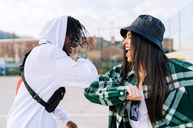 Jovens parceiros multirraciais felizes em moda desgaste cumprimentando uns aos outros com colisão de cotovelo no pavimento urbano — Fotografia de Stock